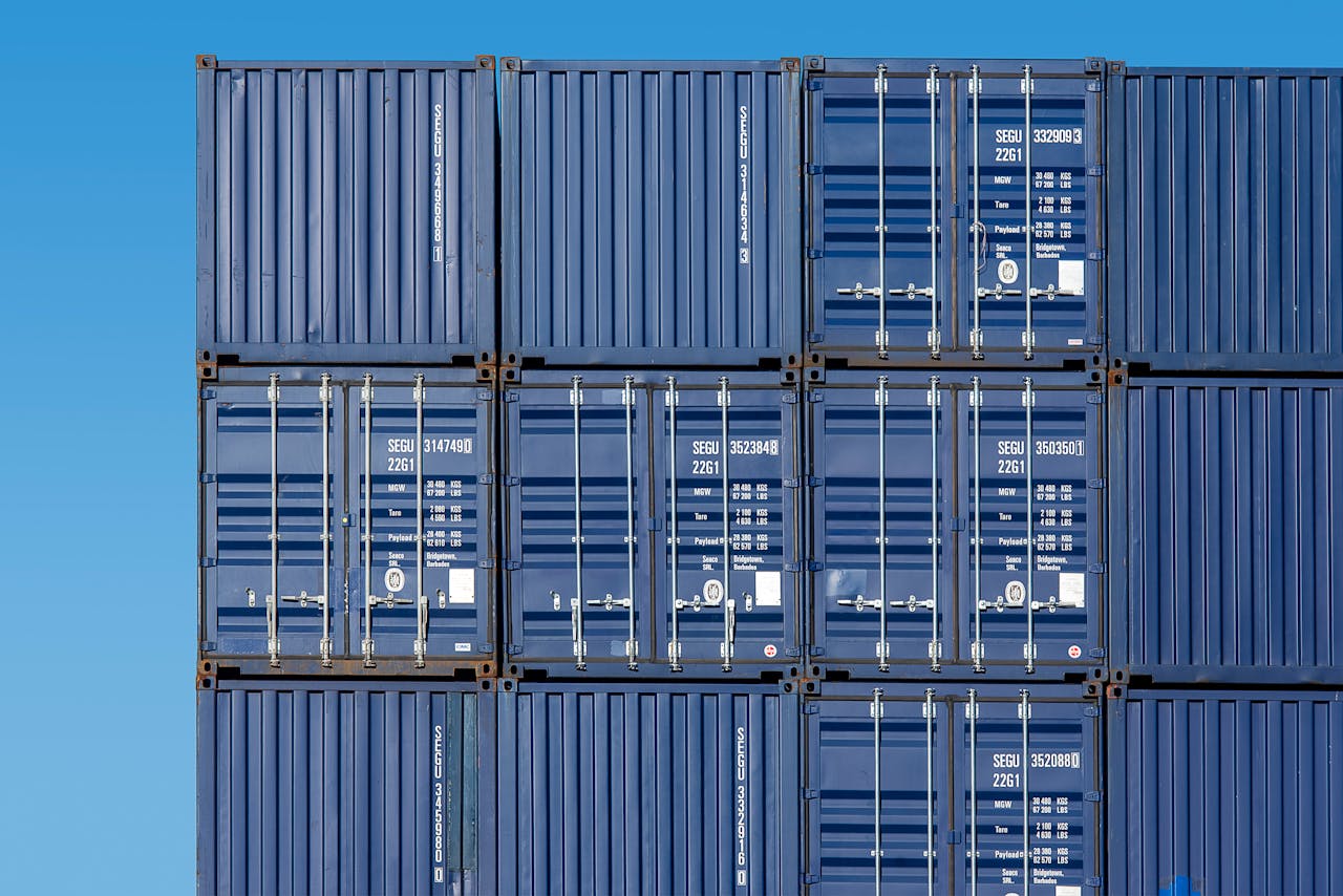services-01 Close-up of blue shipping containers stacked high at Rotterdam Port under a clear blue sky.